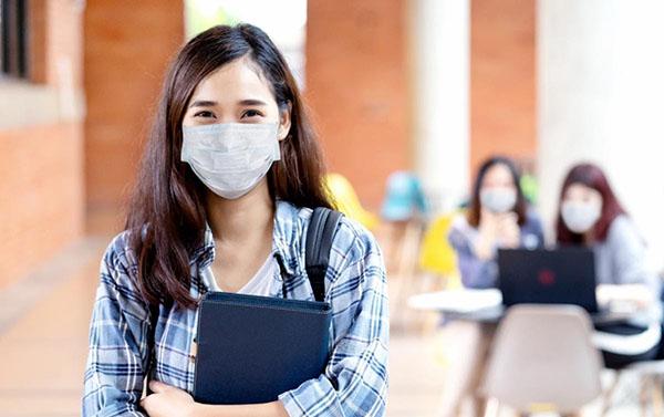 High school student holding books wears a mask while returning to school