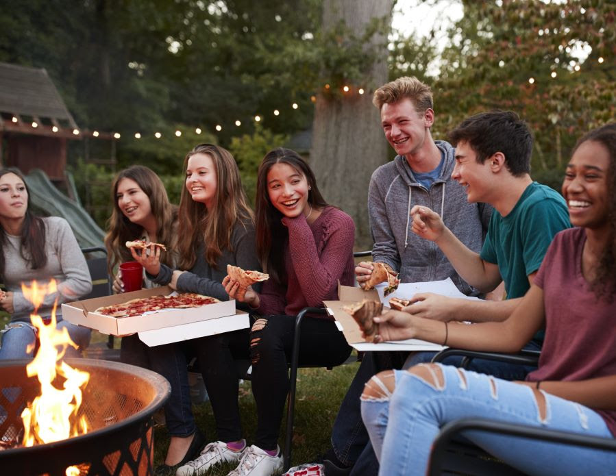 Teens eating pizza around backyard bonfire